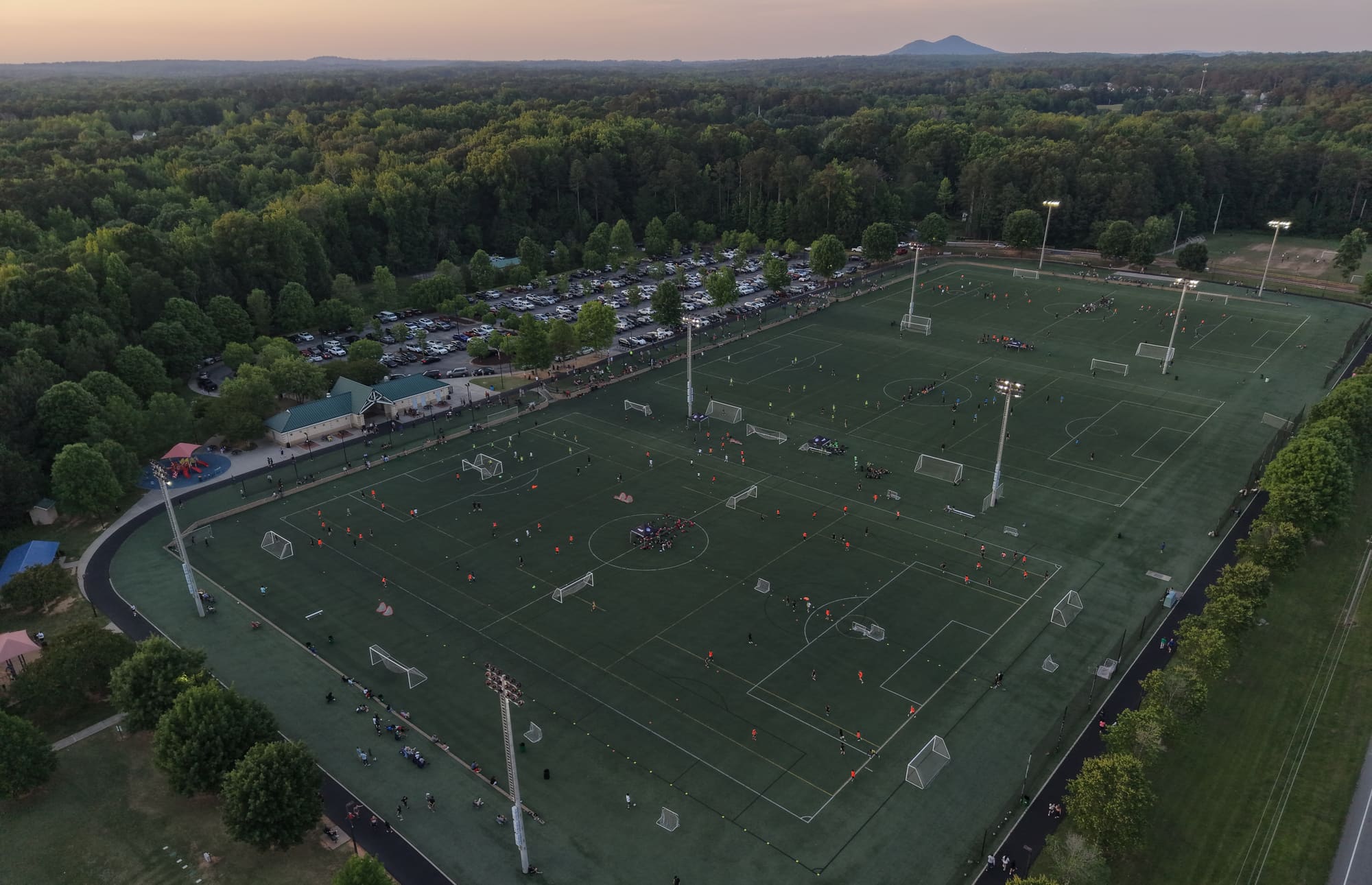 A soccer complex at dusk with games underway under the lights and hills on the horizon